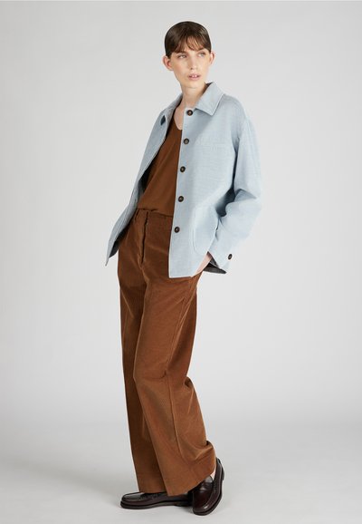 Jasnoniebieska koszula dżinsowa z korduroy i z przodem na guziki; brązowy top na ramiączkach; brązowe szerokie spodnie dżinsowe z korduroy; ciemne buty.