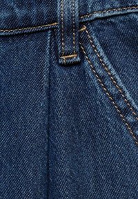 Tissu en denim bleu foncé, présentant un tissage texturé, contrasté par des coutures dorées sur les coutures et un détail de fermeture à boutons.