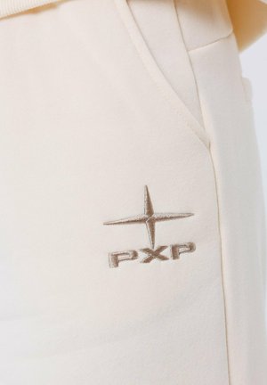 Pantaloni beige chiari con una superficie liscia e una tasca laterale. Presentano un logo "PXP" cucito di colore marrone con un accento a stella.