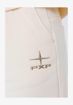 Pantaloni beige chiari con una superficie liscia e una tasca laterale. Presentano un logo "PXP" cucito di colore marrone con un accento a stella.