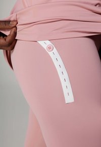 Roze leggings hebben een witte elastische band met een knoopdetail aan de zijkant, gemaakt van een gladde, rekbare stof.