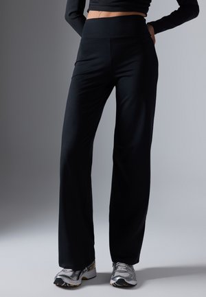 Black, wide-leg pants made of smooth fabric with a high waistband. Paired with grey and black athletic shoes.