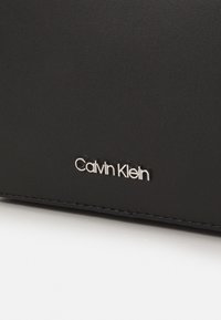 Zwarte leren portemonnee met een gladde textuur en een zilveren "Calvin Klein" logo. Heeft subtiele stiksels langs de randen.