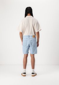 Light beige short-sleeve shirt with a textured pattern, paired with light blue denim shorts featuring a leather patch and back pockets.
