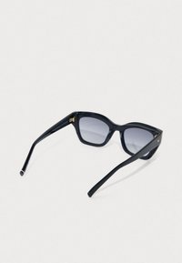 Mustad ristkülikukujulised prillid tumedate gradiendiklaaside ja paksude läikivate raamidega puhkavad valgel pinnal.