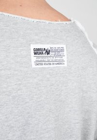 Grijze katoenmix tanktop, met een onafgewerkte halslijn, en een label met details over de stofsamenstelling en onderhoudsinstructies genaaid op de achterkant.