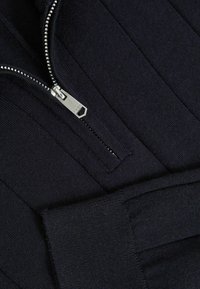 Ciemnoniebieska bluza z zamkiem błyskawicznym, wyposażona w metalowy zamek, o ryflowanej strukturze, dopasowanym kroju oraz wysokim kołnierzu i mankietach.