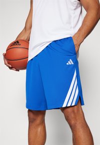 Kék atlétikai rövidnadrág fehér háromcsíkos díszítéssel, könnyű anyagból készült. Laza szabású, oldalsó zsebekkel.