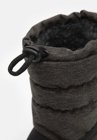 Černá nadýchaná bota s vrchní částí z texturované tkaniny, elastickým zavřením nahoře a měkkým podšívkou. Vyznačuje se odolnou podešví pro dobrou přilnavost a trvanlivost.