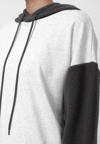 Sudadera ligera gris con acentos de forro polar gris oscuro en las mangas, cordones ajustables, corte casual y textura suave.