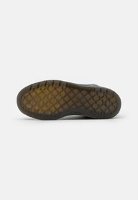 Black rubber boot sole featuring a geometric tread pattern. The sole edges are textured, with a smooth main surface and a transparent gum section.