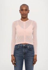Lyserosa langermet cardigan med en knappelukking, med en tettsittende design og gjennomsiktig tekstur, sammen med mørkeblå denimjeans.