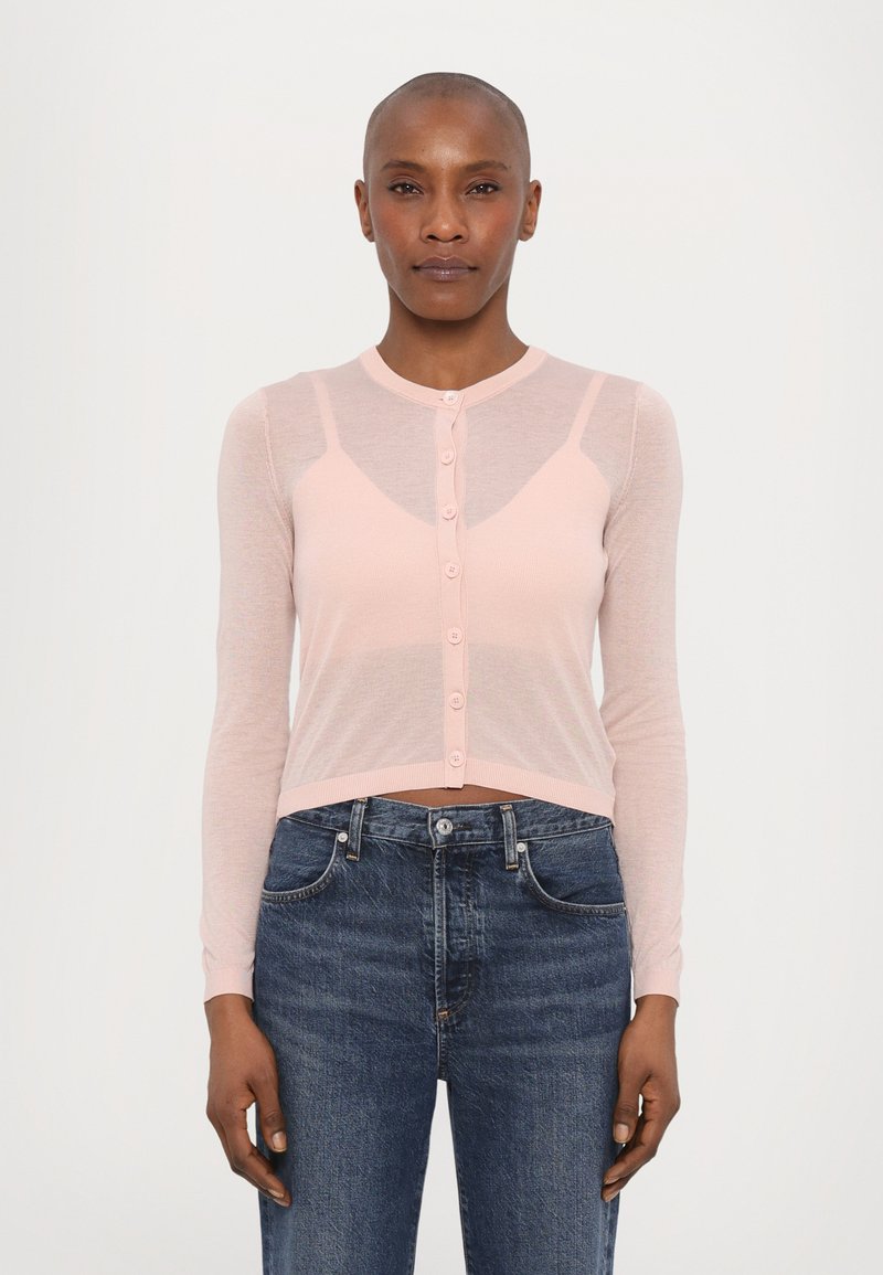 Lyserosa langermet cardigan med en knappelukking, med en tettsittende design og gjennomsiktig tekstur, sammen med mørkeblå denimjeans.