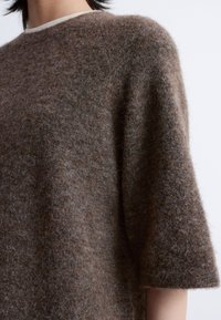 Brauner Wollmischung-Übergrößensweater mit weichem, flauschigem Material, kurzen Ärmeln und einem abgerundeten Halsausschnitt mit einer hellen Einfassung.