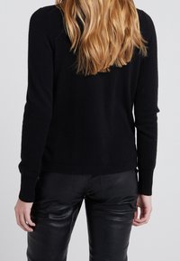 Pull noir en tricot avec manches longues, col rond et coupe ajustée, associé à un pantalon en cuir noir. Texture douce visible.