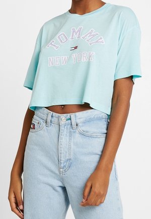 Osoba nosząca jasnoniebieski krótki T-shirt z napisem „Tommy New York” i logo, w połączeniu z jasnoniebieskimi jeansami z wysokim stanem.