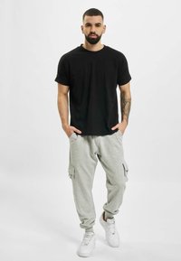 Schwarzes Baumwoll-T-Shirt mit kurzen Ärmeln, kombiniert mit hellgrauen Cargo-Sweatpants mit Seitentaschen, getragen mit weißen Sneakern.