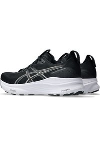 Schwarze Sportschuhe mit einem atmungsaktiven Mesh-Obermaterial, silbernen Akzenten und einer dicken weißen Zwischensohle mit strukturierten Mustern für besseren Halt.
