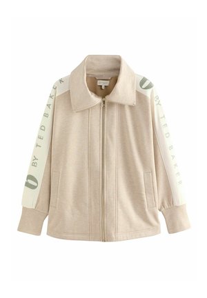Beige zip-up jack met een brede kraag, zachte textuur en contrasterende witte mouwen met groene tekst en logo details. Twee zijzakken.
