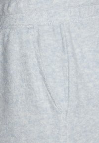 Gaiši zilas faktūras audums ar mīkstu, pūkainu virsmu. Iekļauj sānu kabatas un smalku melnā un pelēkā toņu rakstu, kas piešķir vizuālu interesi.