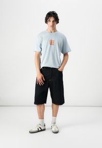Lichtblauw kortinciem t-shirt met de print "FEED YOUR MIND", gecombineerd met donkere denim shorts en witte sneakers met grijze accenten.