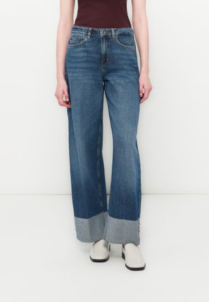Bredvidde denim jeans i blått med en frynset hem, med høy midje og fem lommer, stylet med en mørk topp og lyse sko.