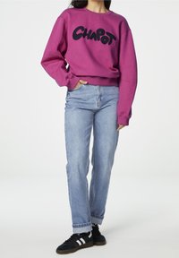 Felpa viola con la scritta "CHAPOT" in nero, abbinata a jeans blu chiaro e sneakers nere con strisce bianche. Look casual.