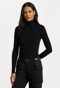 Melna ribota augsta apkakles džemperis ar garām piedurknēm, kombinēts ar melniem cargo biksēm, kas aprīkotas ar strukturētu jostu un vairākiem kabatām.