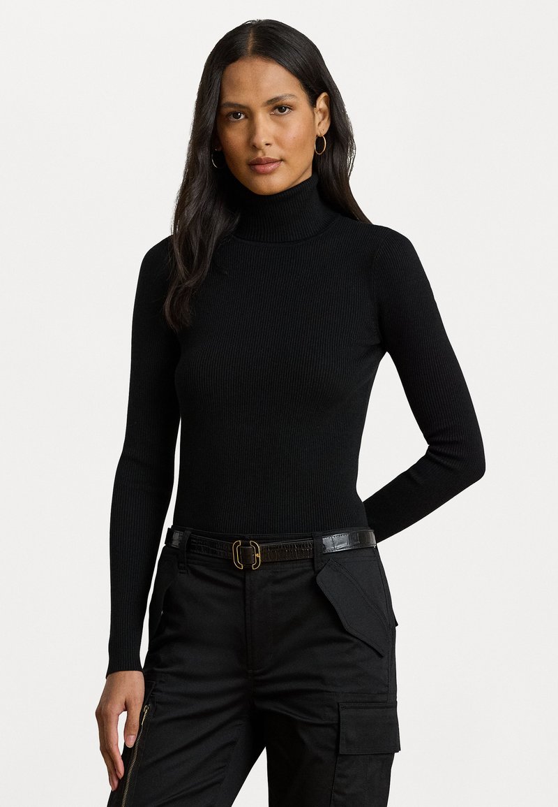 Melna ribota augsta apkakles džemperis ar garām piedurknēm, kombinēts ar melniem cargo biksēm, kas aprīkotas ar strukturētu jostu un vairākiem kabatām.