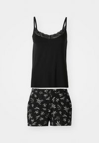 Cămașă fără mâneci neagră cu dantelă, asociată cu pantaloni scurți negri cu un imprimeu botanic alb. Ambele sunt realizate dintr-un material moale și confortabil.
