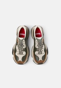 Kaksi vihreää, kermaista ja ruskeaa nahkasneakeria, joissa on paksu pohja. Ominaisuuksia ovat teksturoitu materiaali, nauhat ja punaiset sisäpohjat, joissa on "CAMPER"-logo.