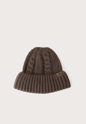 Gorro de punto marrón con patrones de trenzas y un borde doblado que presenta una pequeña etiqueta rectangular con el logo sobre un fondo blanco.