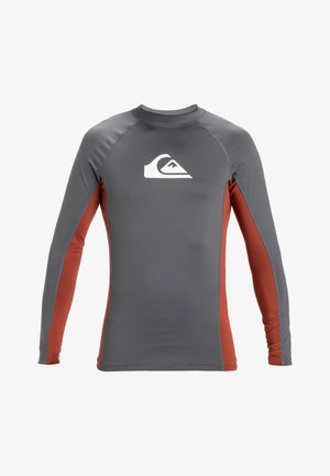 Hallitusülikond halli ja roostepunase värviga, valmistatud venivast kangast. Omab pikkasid varrukaid, ümarat kaelaauku ja valget logo rinnal.