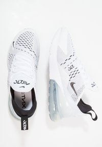 Weiße Sportschuhe mit einem Obermaterial aus Mesh, schwarzen Akzenten und einer sichtbaren Luftpolstersohle. Sie besitzen ein strukturiertes Muster und ein markiertes Logo.