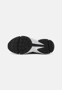 Hvit sneakersåle med en teksturert svart gummiyttersåle med sirkulære mønstre og preget merke.
