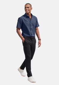 Krekliņš ar īsām piedurknēm, tumši zils, ar pogām, apvienots ar melniem biksēm un baltām sporta apavām. Krekliņam ir strukturēta apkakle un gluda tekstūra.