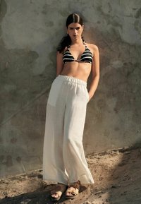 Zwart-wit gestreepte driehoek bikini top, gecombineerd met brede, lichtgewicht, crèmekleurige linnen broeken en tan leren sandalen.