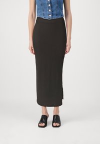Svart ribbad midiklänning med en figurnära siluett och trafslits, kombinerad med svarta öppna sandaler. Denimtoppen har detalj med knappar.