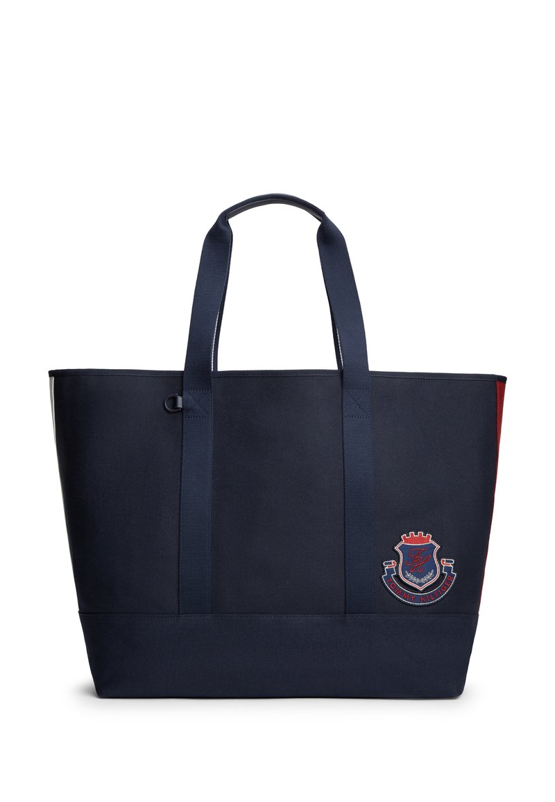 Τσάντα ώμου σε ναυτικό μπλε με δύο λουριά ώμου και ένα έμβλημα Tommy Hilfiger σε κόκκινο, άσπρο και μπλε στην κάτω δεξιά μπροστινή πλευρά.