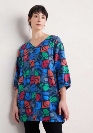 Bunte Tunika aus Stoff mit blauem Hintergrund und roten, grünen und orangefarbenen Blattmustern; V-Ausschnitt und dreiviertel Ärmel.