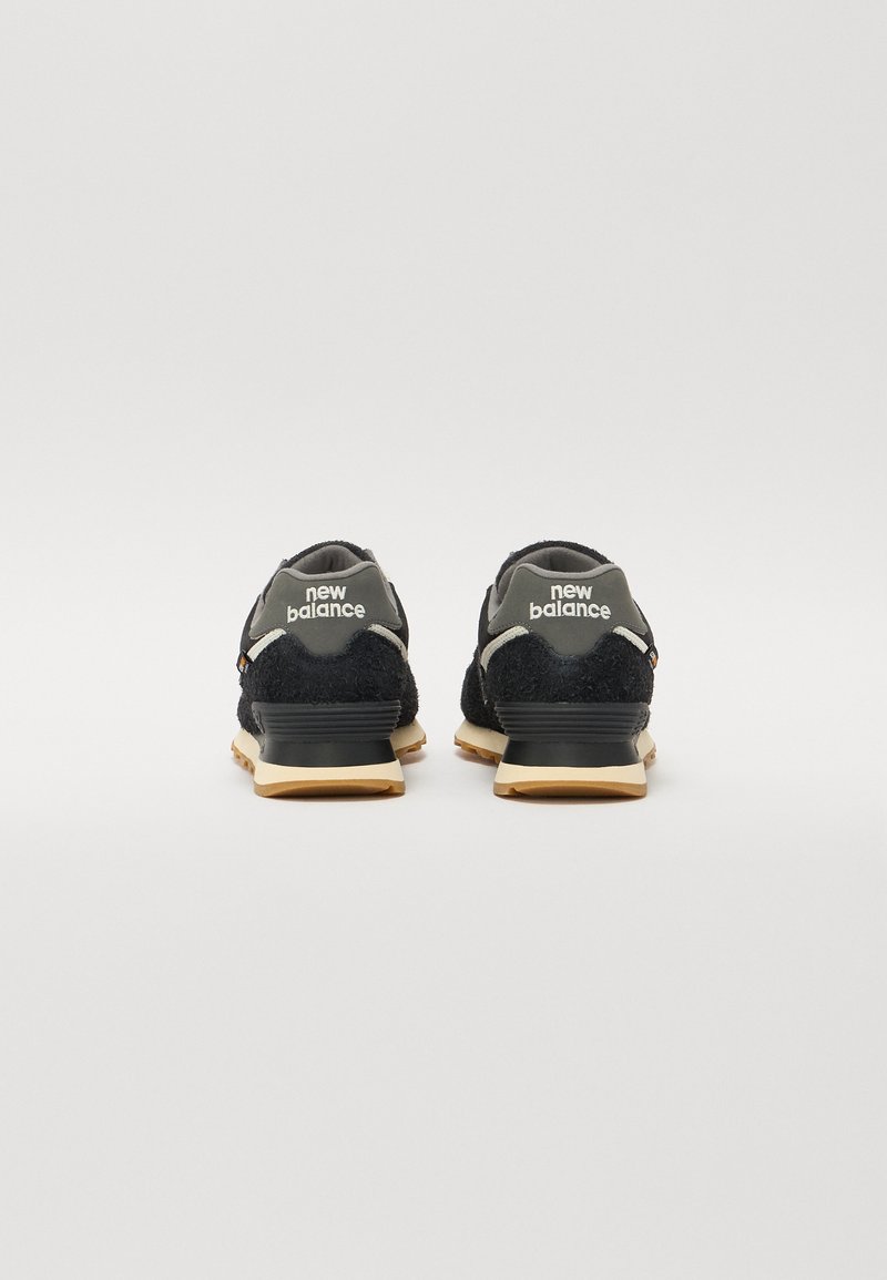 Baskets New Balance noires avec une tige texturée, des accents gris et une semelle en caoutchouc gum. Présente un logo sur le talon et un col doux.