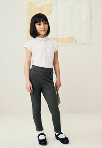 Sive tajice glatke teksture, uparene s bijelom košuljom s ovratnikom. Outfit je upotpunjen crnim cipelama s kopčama.