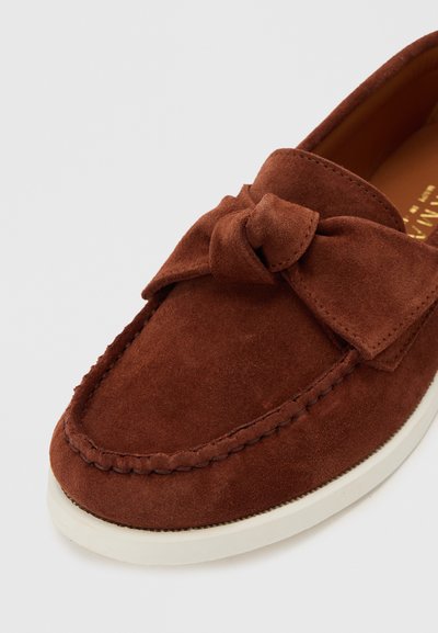Ταμπά σουέντ μοκασίνι με φιόγκο στο επάνω μέρος και λευκή σόλα από καουτσούκ, με εκλεπτυσμένο ράψιμο στην περιοχή της μύτης.