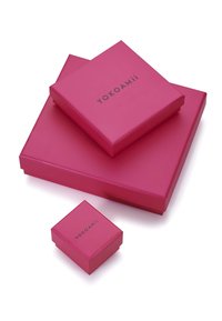 Tre scatole regalo di cartone rosa impilate, con una superficie liscia e una finitura opaca. Ogni scatola presenta il testo "YOKOAMii" in nero.