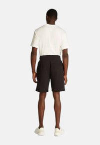 Pantaloni corti neri con una texture liscia e una cintura elastica, abbinati a una maglietta bianca a maniche corte, visti da dietro.