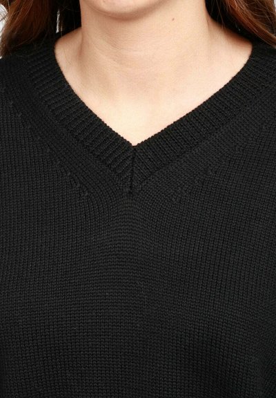 Primo piano di una persona che indossa un maglione nero a collo a V lavorato a maglia, che mostra il colletto e la parte superiore del petto.