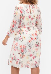Robe florale à design plissé couleur crème, ornée de fleurs roses et jaunes. Elle possède des manches longues, une taille ceinturée et un dos avec une ouverture en forme de goutte.