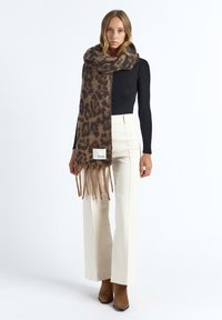 Leopardenmuster-Schal aus weichem Stoff mit fransigen Rändern und weißem Etikett. Das Design wird von warmen Braun- und Beigetönen dominiert.