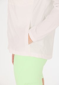 Lättvit jacka med en ficka, i kombination med figurnära neongröna leggings med perforerade detaljer vid fållen.