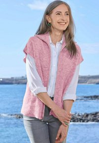 Gilet en tricot rose à manches courtes, avec une fermeture éclair et un col, superposé à une chemise blanche, associé à un pantalon gris. Fond océan.